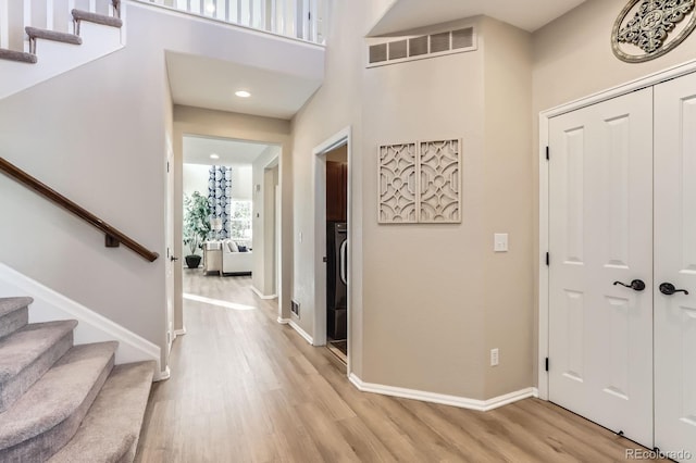foyer entrance with light wood finished floors, stairway, baseboards, recessed lighting, and a high ceiling