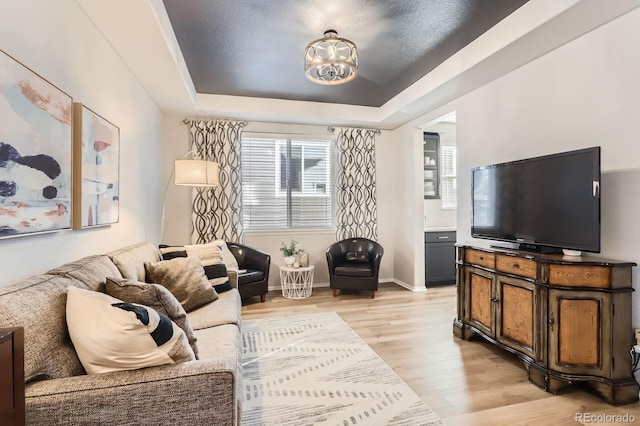 living room featuring light wood-style flooring, a chandelier, a tray ceiling, and baseboards