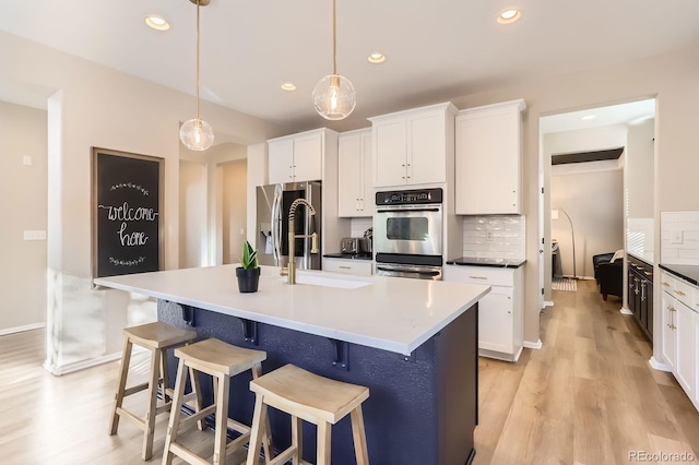 kitchen with appliances with stainless steel finishes, a sink, light wood-style floors, recessed lighting, and white cabinetry
