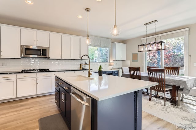kitchen with stainless steel appliances, a sink, decorative backsplash, light wood-style floors, and white cabinetry