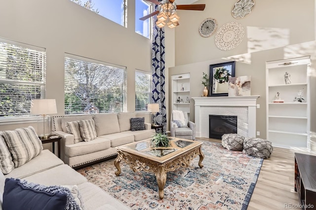living room featuring a ceiling fan, plenty of natural light, a towering ceiling, wood finished floors, and a glass covered fireplace