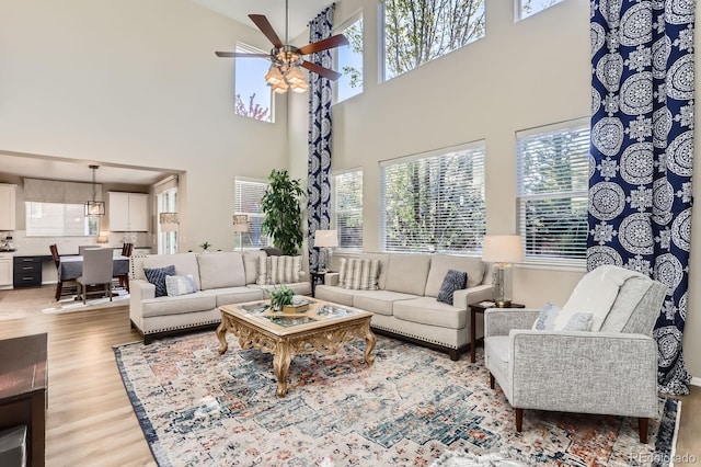 living area featuring a ceiling fan, light wood-style flooring, and a towering ceiling