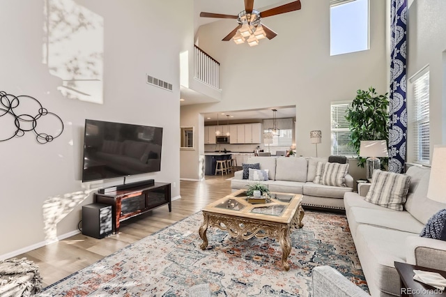 living area featuring ceiling fan, light wood finished floors, a towering ceiling, and baseboards