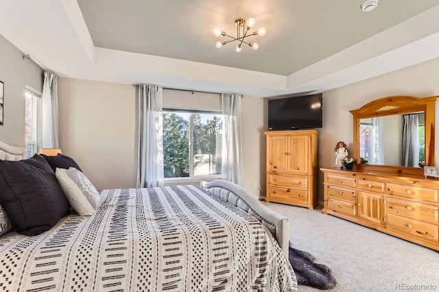 bedroom featuring multiple windows, light carpet, a raised ceiling, and a chandelier