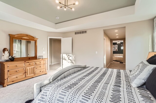 bedroom with light colored carpet, a chandelier, a tray ceiling, ensuite bathroom, and baseboards