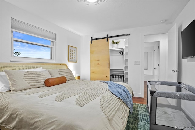 bedroom with a walk in closet, a closet, a barn door, and wood-type flooring