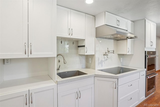 6121 W 108th Ave, Westminster, CO 80020 - kitchen featuring under cabinet range hood, black electric stovetop, double oven, light countertops, and white cabinetry
