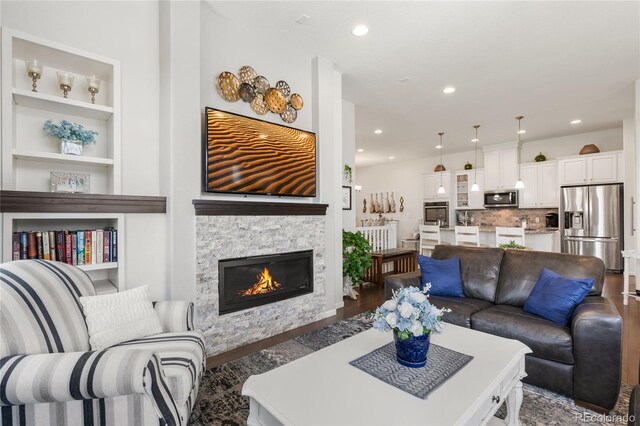 25049 E Alder Dr, Aurora, CO 80016 - living room featuring recessed lighting, wood finished floors, built in shelves, and a stone fireplace