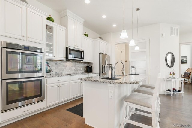 25049 E Alder Dr, Aurora, CO 80016 - kitchen featuring appliances with stainless steel finishes, decorative backsplash, white cabinets, a center island with sink, and recessed lighting