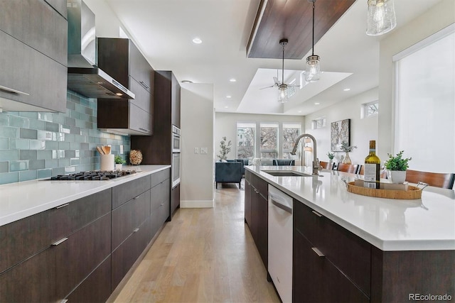 kitchen with wall chimney range hood, sink, decorative light fixtures, a large island, and stainless steel appliances