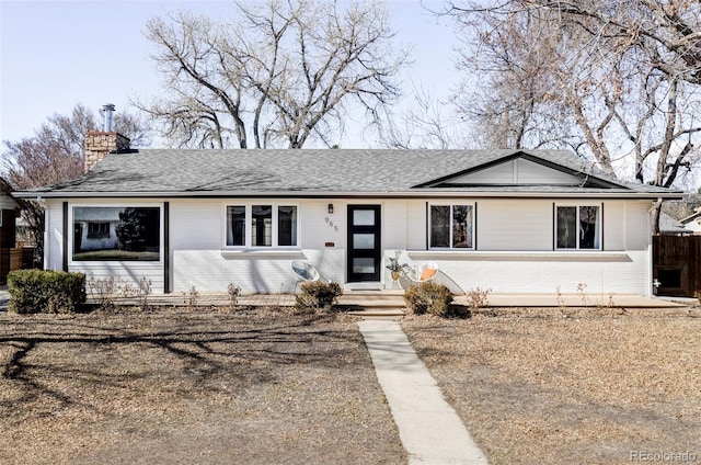 ranch-style home featuring roof with shingles, brick siding, a chimney, and fence