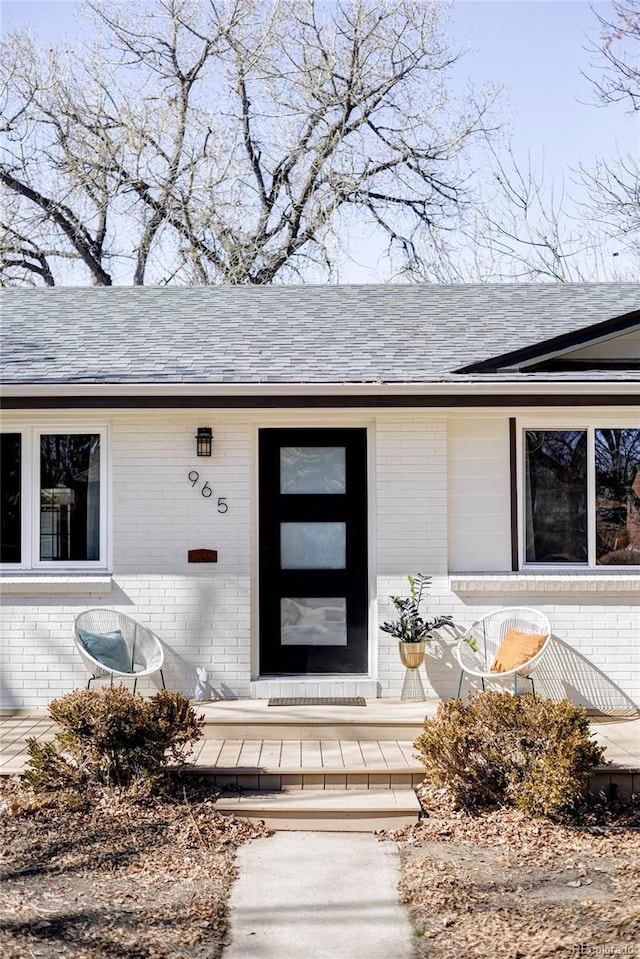 doorway to property featuring brick siding and roof with shingles