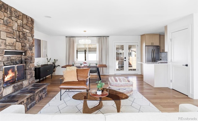 living area featuring french doors, a stone fireplace, and light wood finished floors