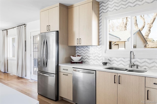 kitchen featuring light countertops, appliances with stainless steel finishes, a sink, and light brown cabinetry