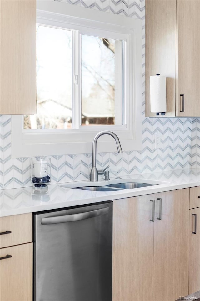 kitchen with backsplash, light countertops, stainless steel dishwasher, light brown cabinets, and a sink