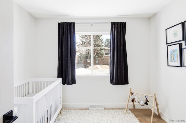 bedroom featuring a crib, wood finished floors, visible vents, and baseboards