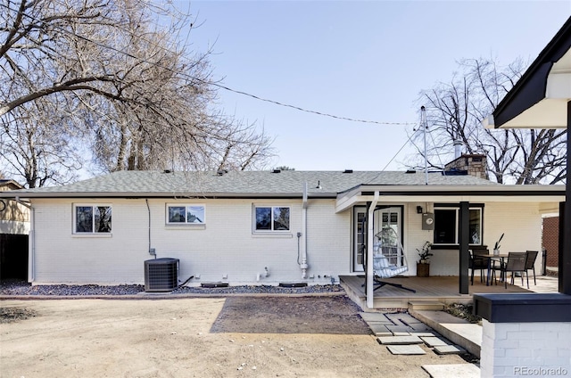 rear view of property featuring roof with shingles, central AC unit, a chimney, and brick siding