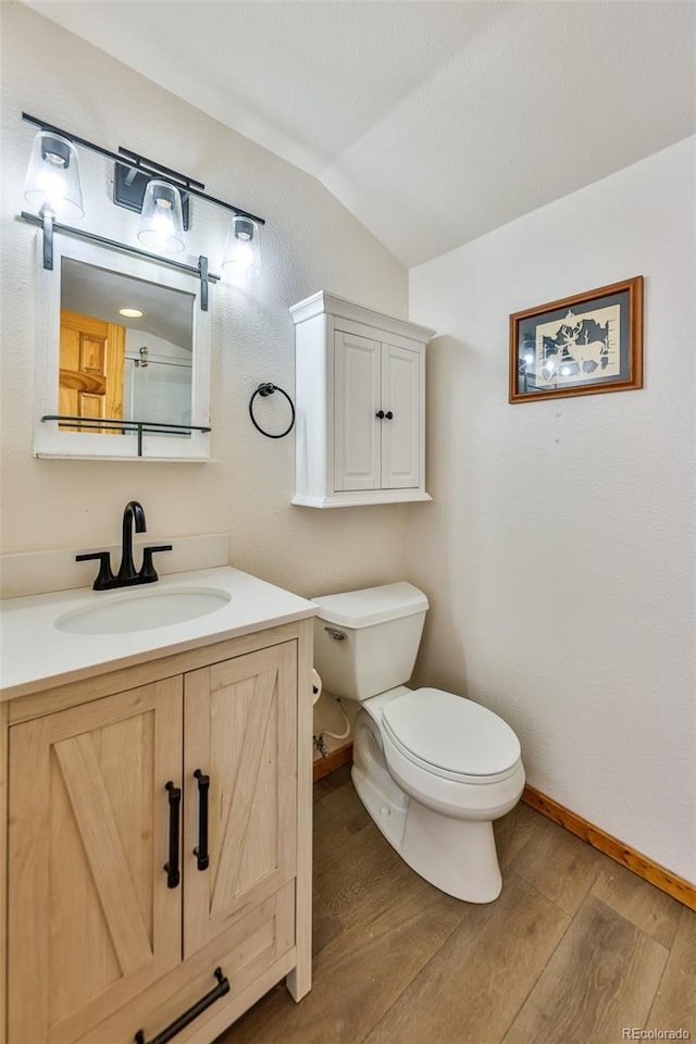 bathroom featuring toilet, hardwood / wood-style flooring, vanity, and vaulted ceiling