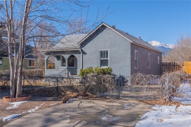 view of front of property with a fenced front yard, a mountain view, roof with shingles, and stucco siding