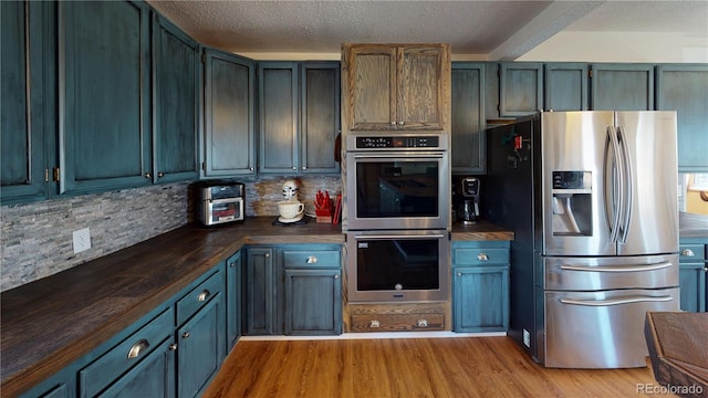 kitchen featuring a textured ceiling, light wood-type flooring, appliances with stainless steel finishes, butcher block countertops, and backsplash