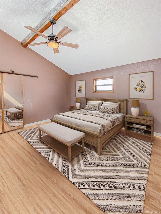 bedroom featuring lofted ceiling with beams, hardwood / wood-style flooring, ceiling fan, and a textured ceiling