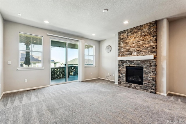 unfurnished living room with a textured ceiling, carpet flooring, and a stone fireplace