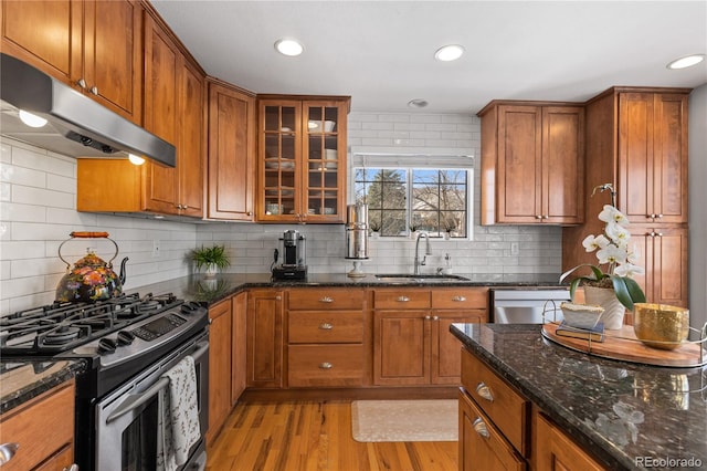 kitchen featuring a sink, under cabinet range hood, appliances with stainless steel finishes, brown cabinetry, and light wood finished floors