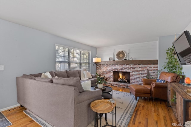 living room with visible vents, a brick fireplace, baseboards, and wood finished floors