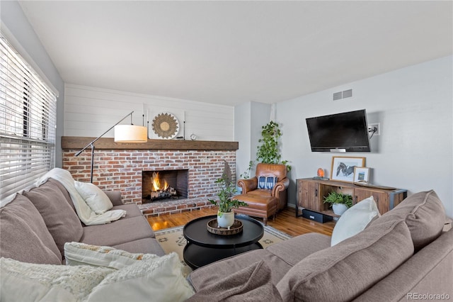 living room with visible vents, a brick fireplace, and wood finished floors