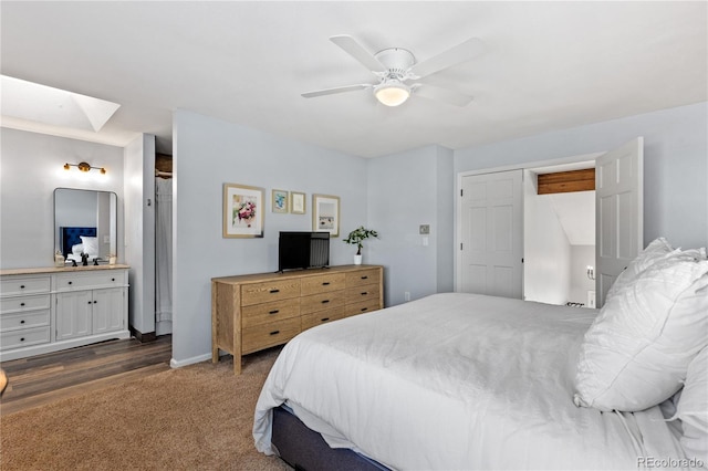 bedroom featuring a ceiling fan, ensuite bath, dark carpet, a skylight, and baseboards