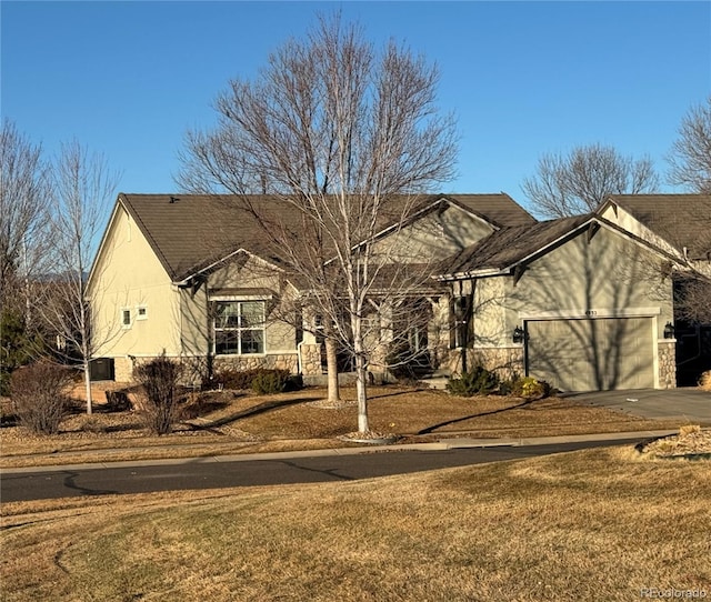 ranch-style house featuring aphalt driveway, a garage, stone siding, stucco siding, and a front yard