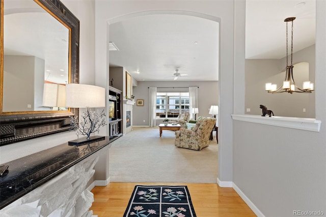 interior space featuring arched walkways, light colored carpet, light wood-style flooring, a chandelier, and baseboards