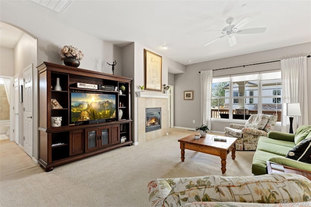 carpeted living area with a ceiling fan, a tile fireplace, arched walkways, and baseboards