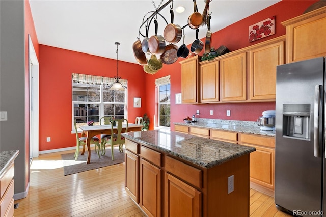 kitchen featuring stainless steel fridge with ice dispenser, hanging light fixtures, a center island, dark stone counters, and light wood finished floors