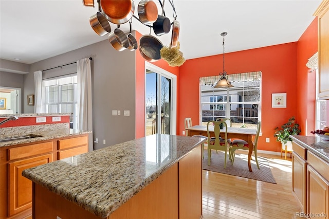 kitchen featuring light stone counters, a sink, hanging light fixtures, a center island, and light wood finished floors