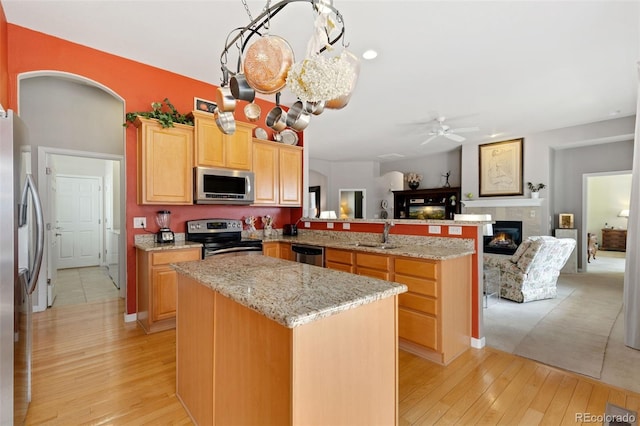 kitchen featuring a tile fireplace, open floor plan, a peninsula, stainless steel appliances, and a sink