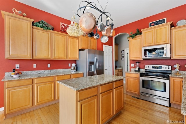 kitchen with arched walkways, appliances with stainless steel finishes, light wood-style floors, a kitchen island, and light stone countertops