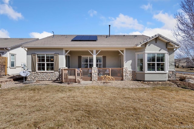 rear view of house with a tile roof, stucco siding, a lawn, roof mounted solar panels, and stone siding