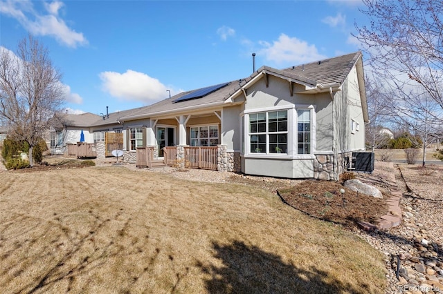 rear view of property featuring covered porch, solar panels, stone siding, a lawn, and stucco siding