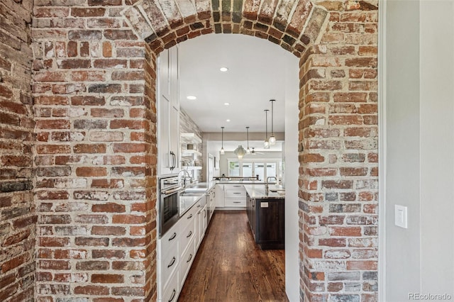 kitchen featuring oven, hanging light fixtures, brick wall, dark wood finished floors, and white cabinetry