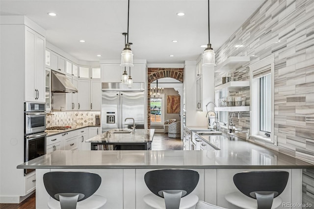 kitchen featuring appliances with stainless steel finishes, white cabinets, a breakfast bar area, and under cabinet range hood