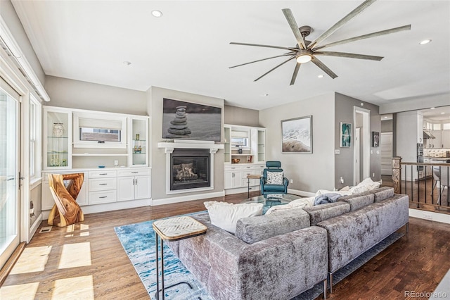 living area with a ceiling fan, a glass covered fireplace, wood finished floors, and recessed lighting