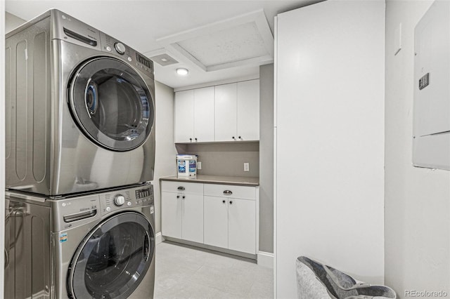 washroom with cabinet space, stacked washer and dryer, light tile patterned flooring, and attic access