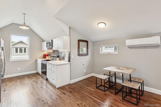 kitchen with light countertops, stainless steel appliances, white cabinetry, a wall unit AC, and vaulted ceiling