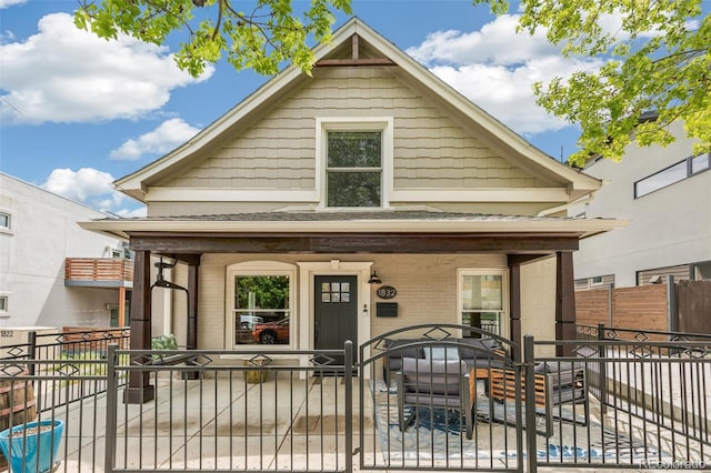 view of front of home with brick siding, a gate, a fenced front yard, and a porch