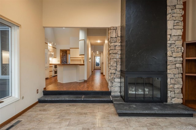 living room featuring a high ceiling, a fireplace, baseboards, and visible vents