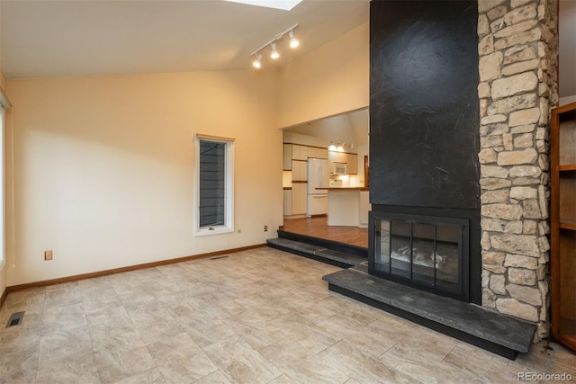 unfurnished living room with a stone fireplace, baseboards, rail lighting, and visible vents