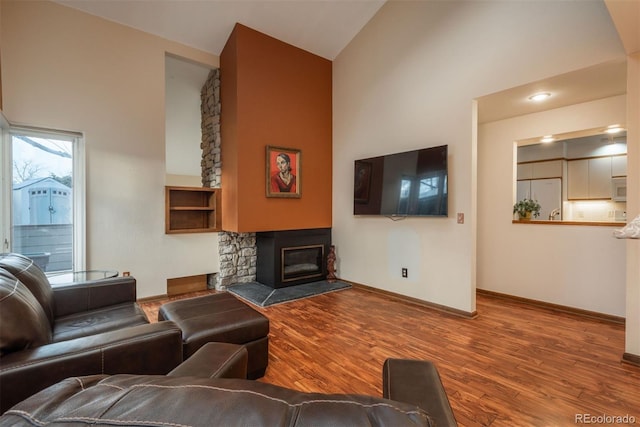 living room featuring high vaulted ceiling, a fireplace, baseboards, and wood finished floors