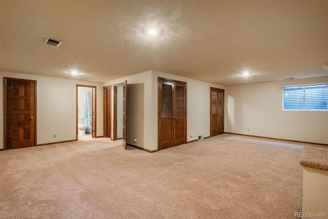 basement with a textured ceiling, baseboards, carpet, and visible vents
