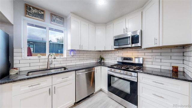 kitchen with white cabinets, stainless steel appliances, dark stone counters, and sink